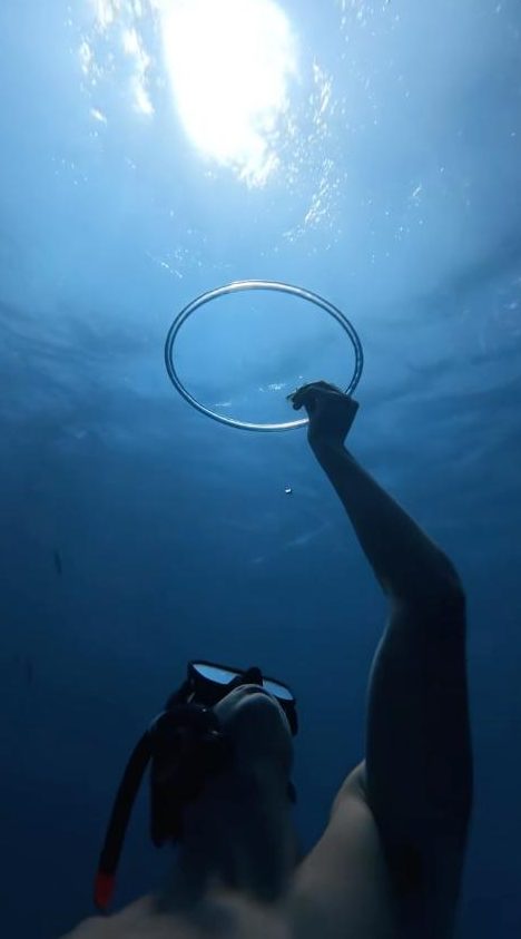 George reaching up to touch a bubble ring under sunlit blue water